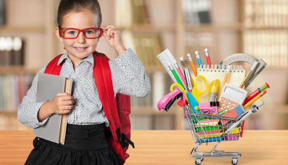 Schülerin mit roter Brille sitzt neben Einkaufswagen voll mit Schulartikel