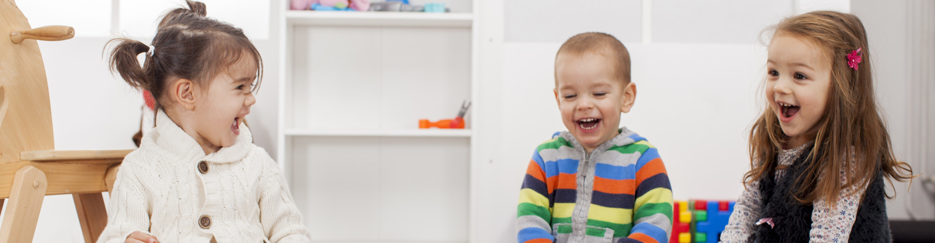 Zwei kleine Mädchen und ein Bub sitzen im Kindergarten und lachen